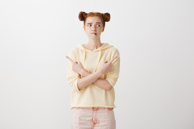 Free photo anxious insecure redhead girl facing choice, pointing fingers sideways