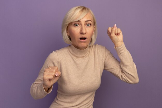 Anxious pretty blonde slavic woman keeps fists on purple