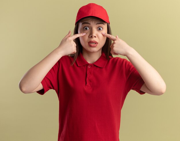 Anxious pretty delivery woman in uniform puts fingers on eyelids