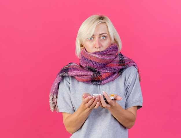 Free photo anxious young blonde ill slavic woman wearing scarf holds packs of medical pills