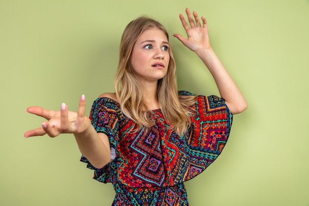 Free photo anxious young blonde slavic girl standing with raised hands and looking at side