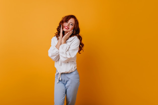 Appealing long-haired girl posing with cute smile. Graceful white young lady standing on yellow wall.