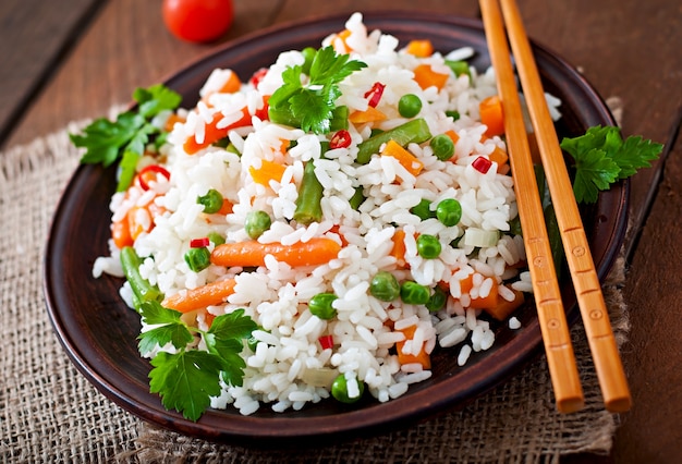 Free photo appetizing healthy rice with vegetables in white plate on a wooden table.