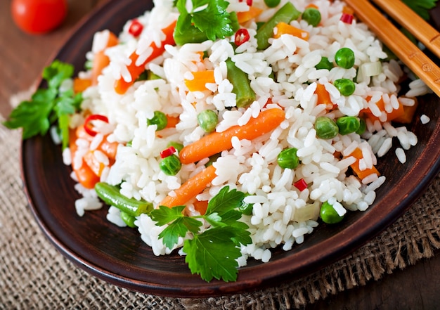 Appetizing healthy rice with vegetables in white plate on a wooden table.