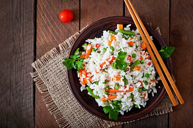 Appetizing healthy rice with vegetables in white plate on a wooden table.