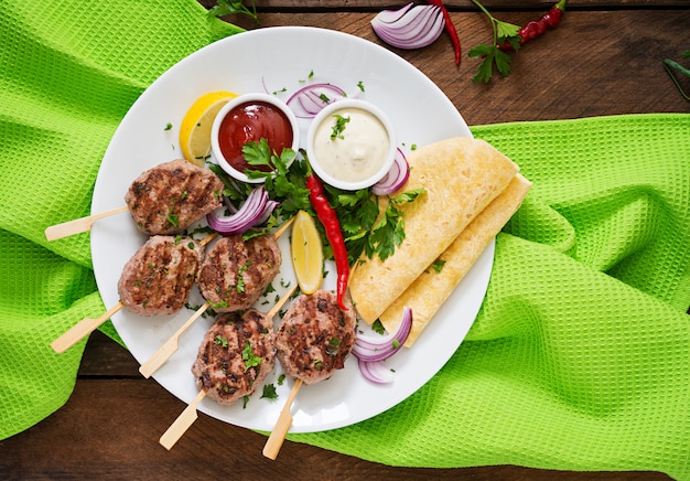 Free photo appetizing kofta kebab (meatballs) with sauce and tortillas tacos on a white plate.