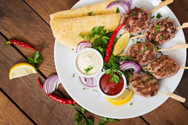 Free photo appetizing kofta kebab (meatballs) with sauce and tortillas tacos on a white plate.