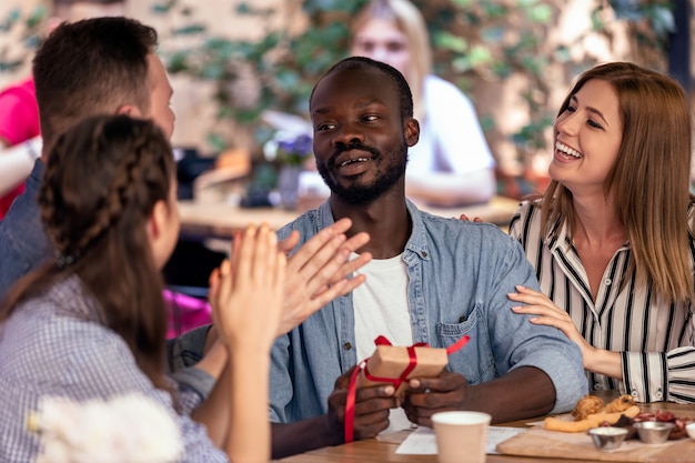 Applause and gifts  for an african boy from his caucasian friends at the cozy cafe