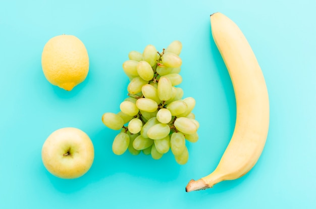 Apple lemon grapes and banana on turquoise surface