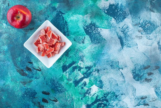 Apple and red marmalade in a bowl, on the blue table.