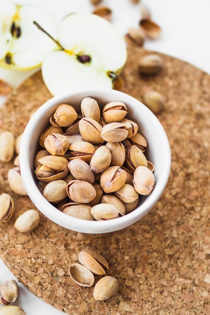 Apple with bowl of pistachio nuts on cork coaster