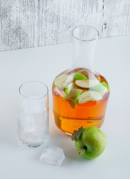 Apple with drink, ice cubes in glass on white and grungy, high angle view.