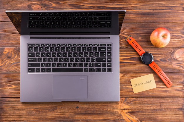 Free photo apple; wristwatch; laptop and gold card on wooden desk