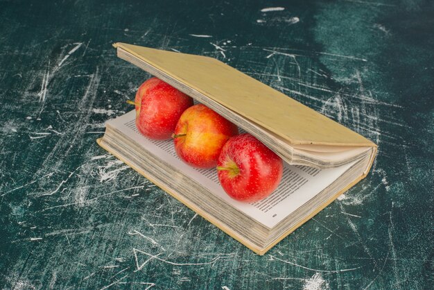 Apples inside a book on marble surface with knife.