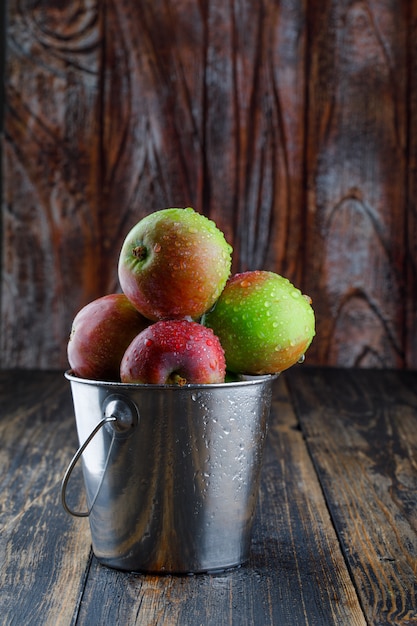 Free Photo apples in a mini bucket on old wooden background. side view.