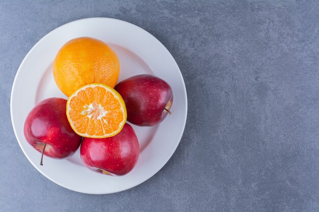 Apples and orange on plate on marble table.