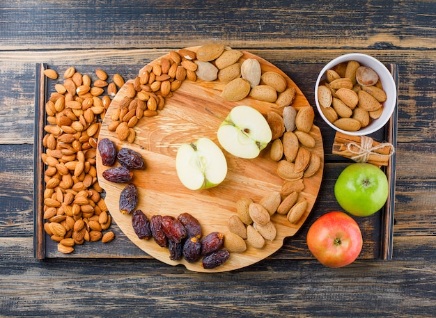 Apples and slices on a cutting board with cinnamon sticks, dates and almonds top view on wooden piece and wooden