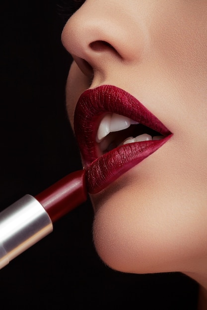 Applying red lipstick on lips in close up photo on black background. Beauty and make up