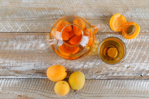 Apricot tea in teapot and glass mug with apricots top view on a wooden table