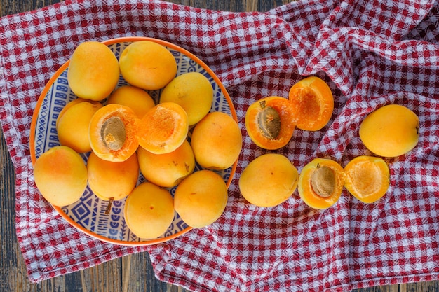 Free photo apricots in a plate flat lay on picnic cloth and wooden table