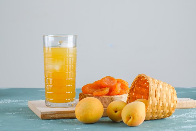 Apricots with dried apricots, cutting board, juice in a basket, side view.