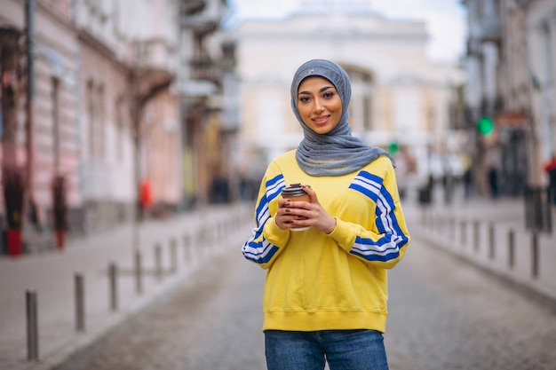 Free photo arabian woman in hijab ouside in the street drinking coffee