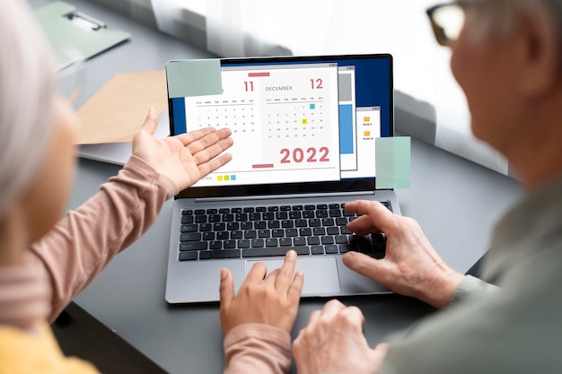 Free Photo arabic woman teaching senior man to use calendar laptop sitting at desk