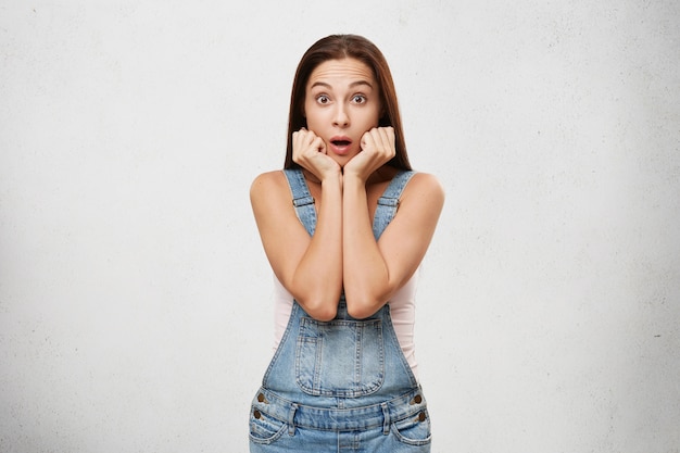 Are you serious? Surprised bug eyed attractive young brunette female customer or student holding hands at her face looking in full disbelief after receiving astonishing shocking news. Body language