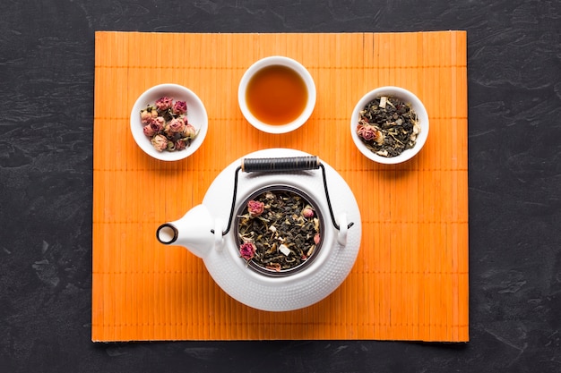 Free Photo aromatic herbal tea and ingredient with white ceramic teapot on orange place mat