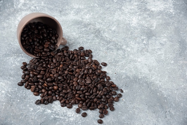 Aromatic roasted coffee beans out of cup on marble surface.