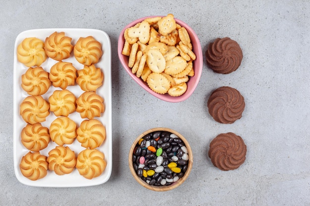 Arrangement of cookies on and off platter with bowls of crackers and candies in the middle on marble background. High quality photo