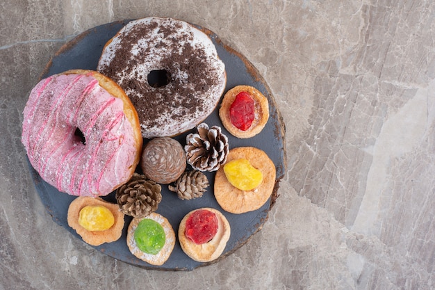 Arrangement of pine cones, donuts and cookies on a board on marble. 