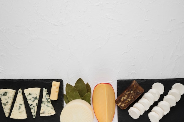 Free photo arrangement of various cheese on black slate with bay leaves at corner of the white surface