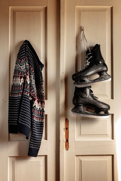 Free Photo arrangement with ice skates and sweater hanging on the door