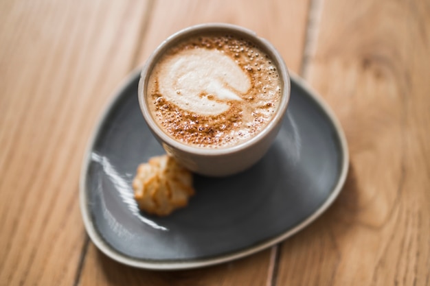 The art of cappuccino on ceramic cup with cookie over the wooden table