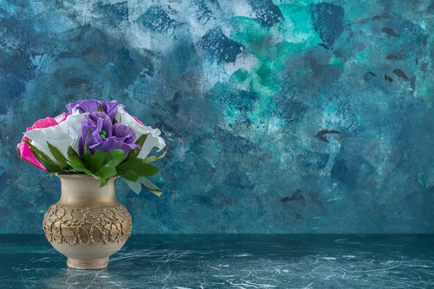 Artificial colorful flower in a vase , on the blue background.