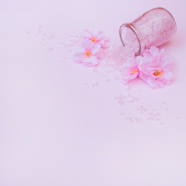 Artificial flowers and spilled salt from jar on pink background