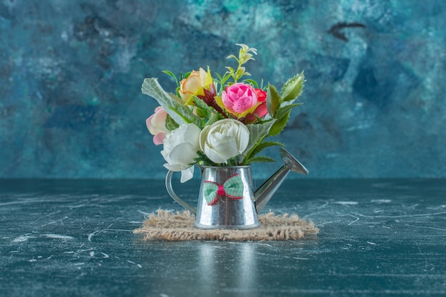 Artificial flowers in a watering can , on the blue background.