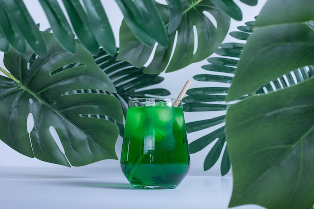 Free photo artificial green leaves and glass of juice on white table.