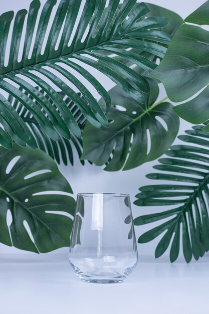 Artificial leaves and empty glass on white surface.