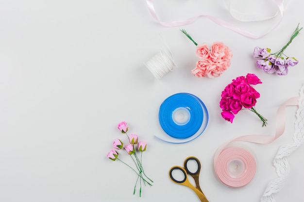 An artificial roses; scissor with blue and pink ribbon on white background