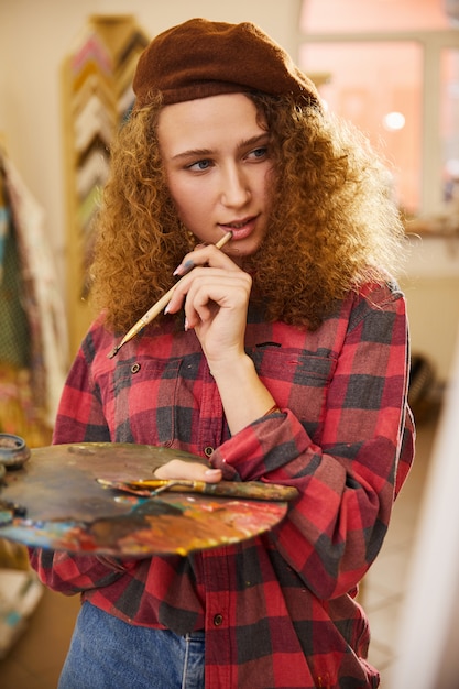 Artist holds a brush and is thinking about during her work