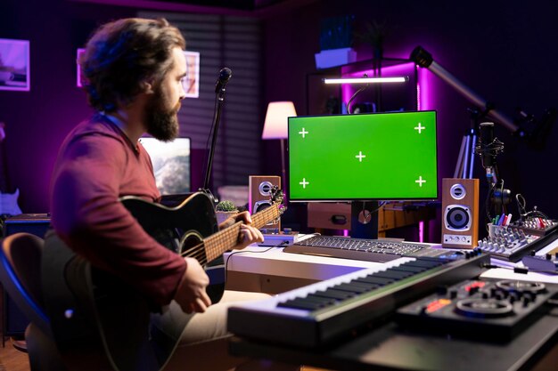 Artist learning to play guitar with internet lessons on greenscreen monitor