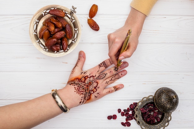 Artist making mehndi on womans hand near dates fruit