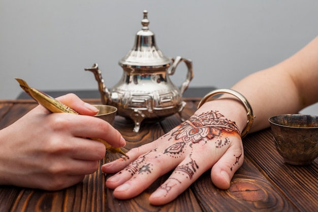 Free photo artist making mehndi on womans hand near teapot