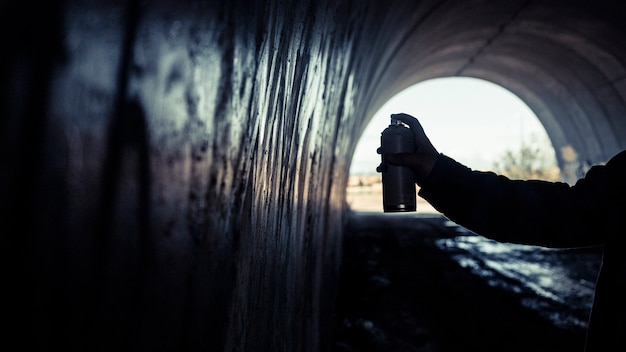 Free photo artist's hand painting graffiti with spray can inside tunnel