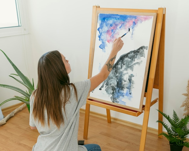 Free photo artist woman painting on canvas  from behind shot