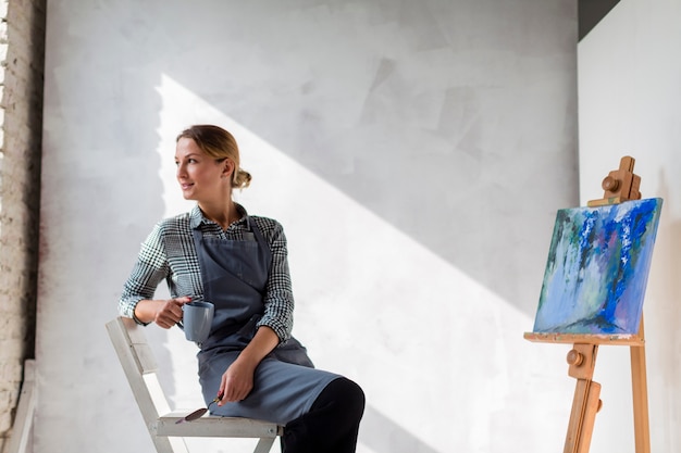 Free photo artist woman posing on chair with canvas