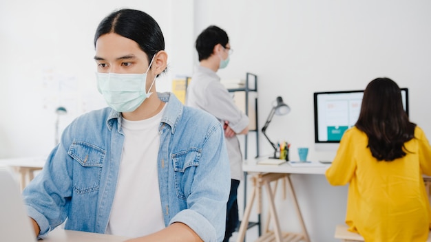 Asia businessman entrepreneur wearing medical face mask for social distancing in new normal situation for virus prevention while using laptop back at work in office. Lifestyle after corona virus.