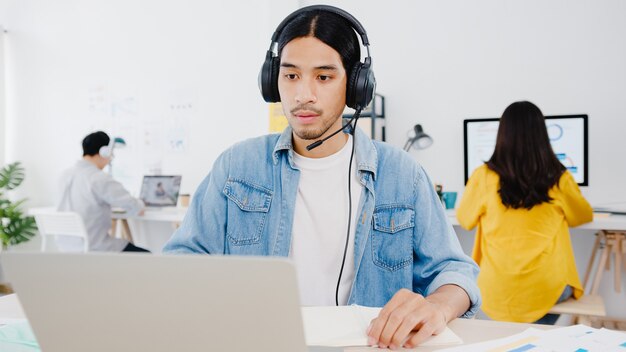 Asia businessman social distancing in new normal situation for virus prevention using laptop presentation to colleague about plan in video call while work in home office. Lifestyle after corona virus.